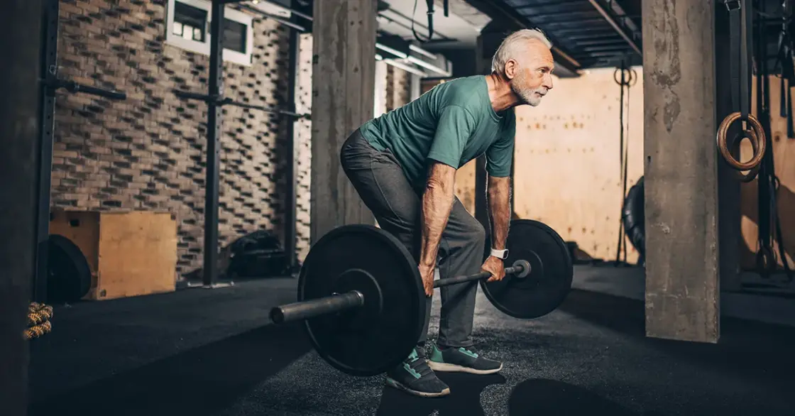 Active elderly man doing a deadlift workout in a gym area of a gym