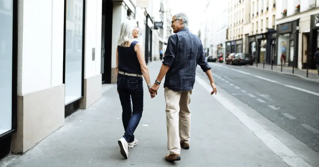 A couple walks down a city street on the sidwalk holding hands