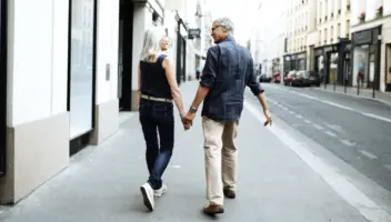 A couple walks down a city street on the sidwalk holding hands